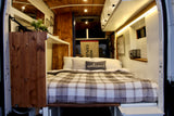 Cozy RV rental interior: a comfy plaid bed, warm wood paneling, and bright ambient lighting for your travels.