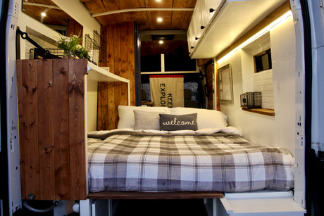 Cozy RV rental interior: a comfy plaid bed, warm wood paneling, and bright ambient lighting for your travels.