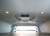 RV rental interior featuring a white paneled ceiling with AC unit, recessed lights, and a cozy bed looking out bright open rear doors.
