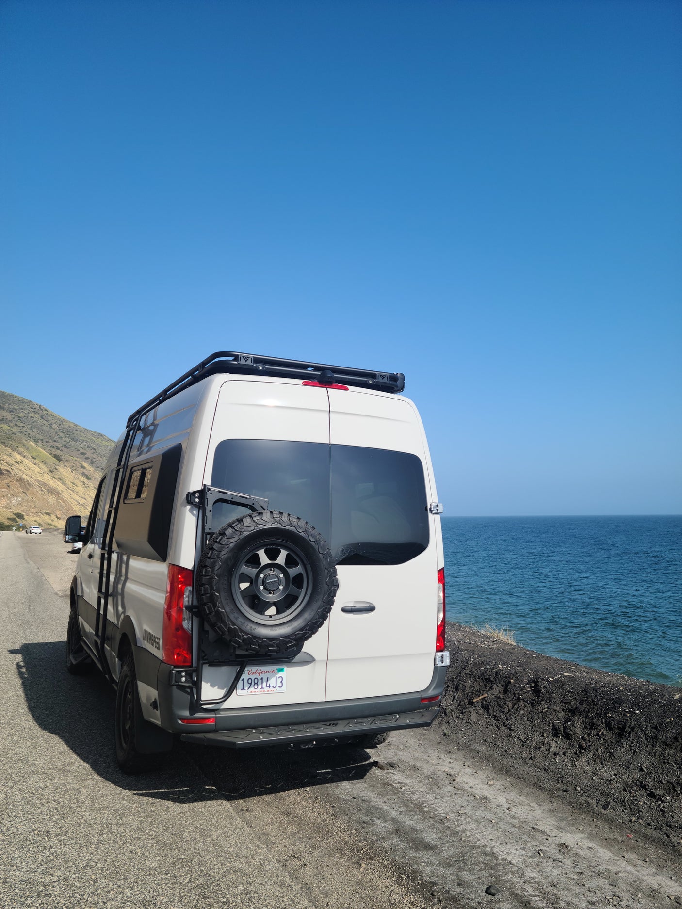 Explore coastal beauty with an RV rental. This white camper van is parked seaside, offering stunning ocean views under a clear sky.