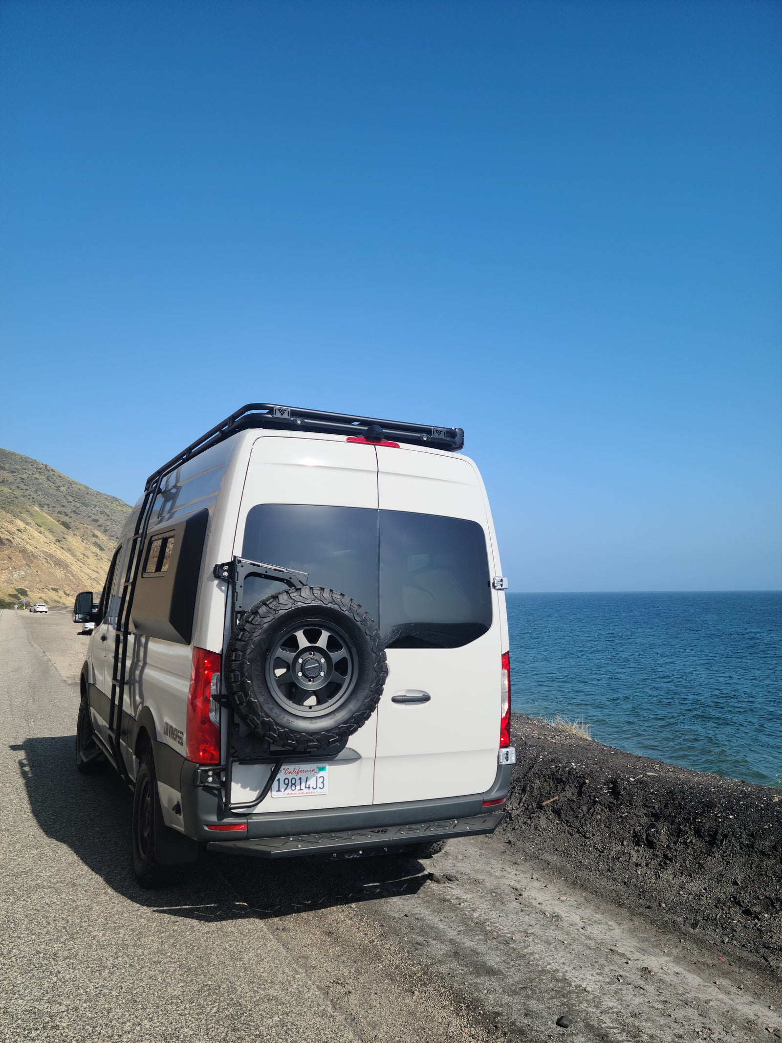 Explore coastal beauty with an RV rental. This white camper van is parked seaside, offering stunning ocean views under a clear sky.