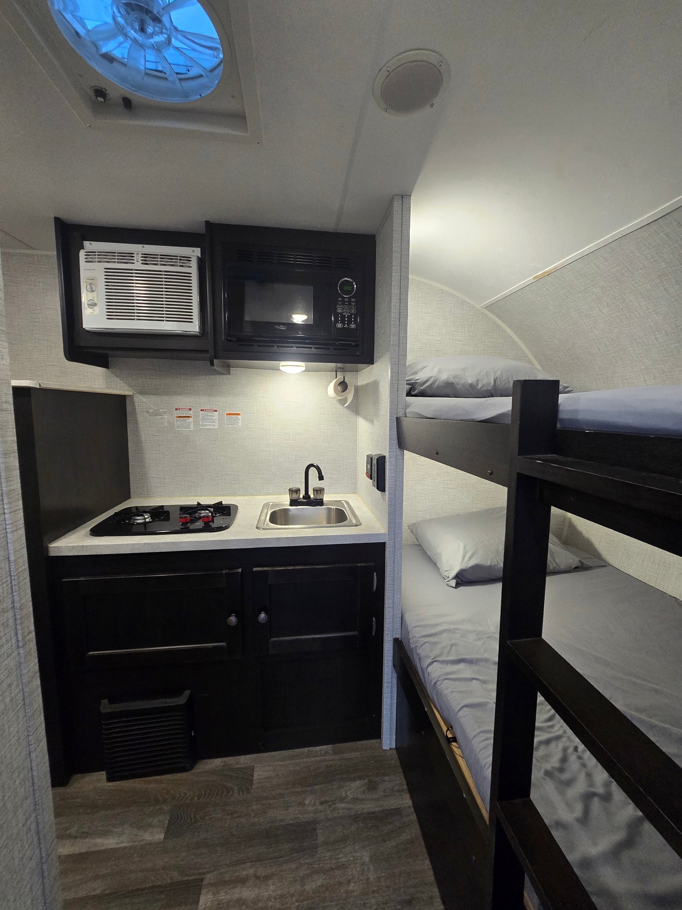 Cozy RV rental interior: kitchenette with stove, sink, microwave, and AC, plus comfortable bunk beds for compact travel.