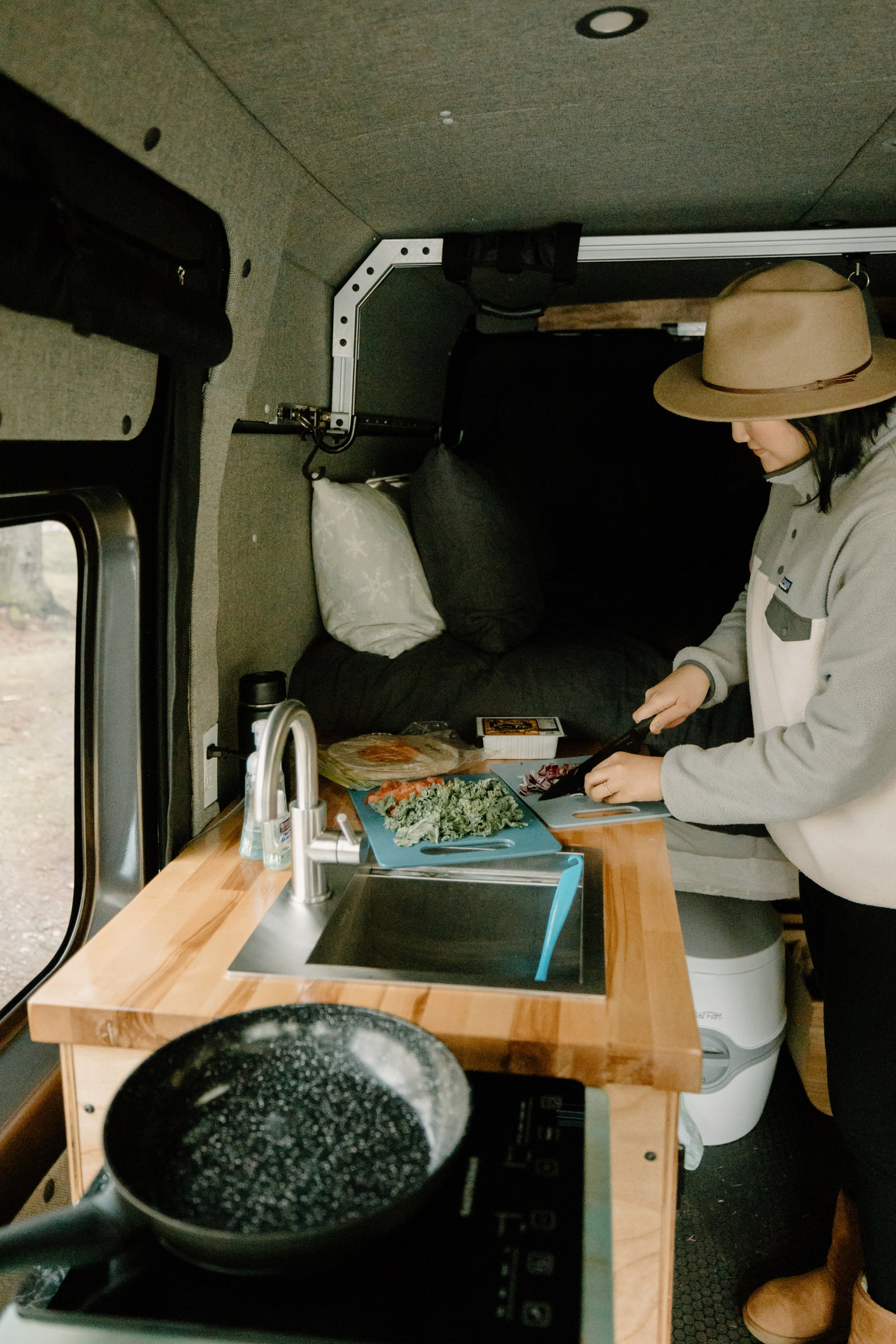 Preparing a meal in an RV rental. A person chops veggies on a compact kitchen counter, showing efficient van life cooking.