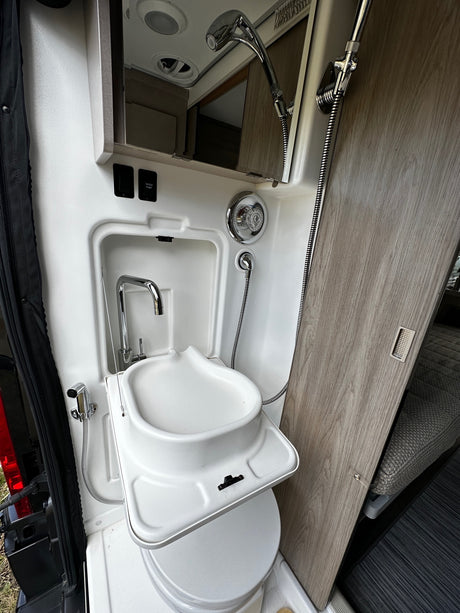 RV rental camper van interior: compact wet bath with a sink, pull-out shower, and portable toilet.