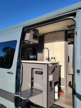 Inside a modern RV rental: compact kitchen with sink, control panel, and pull-out table for efficient mobile living.