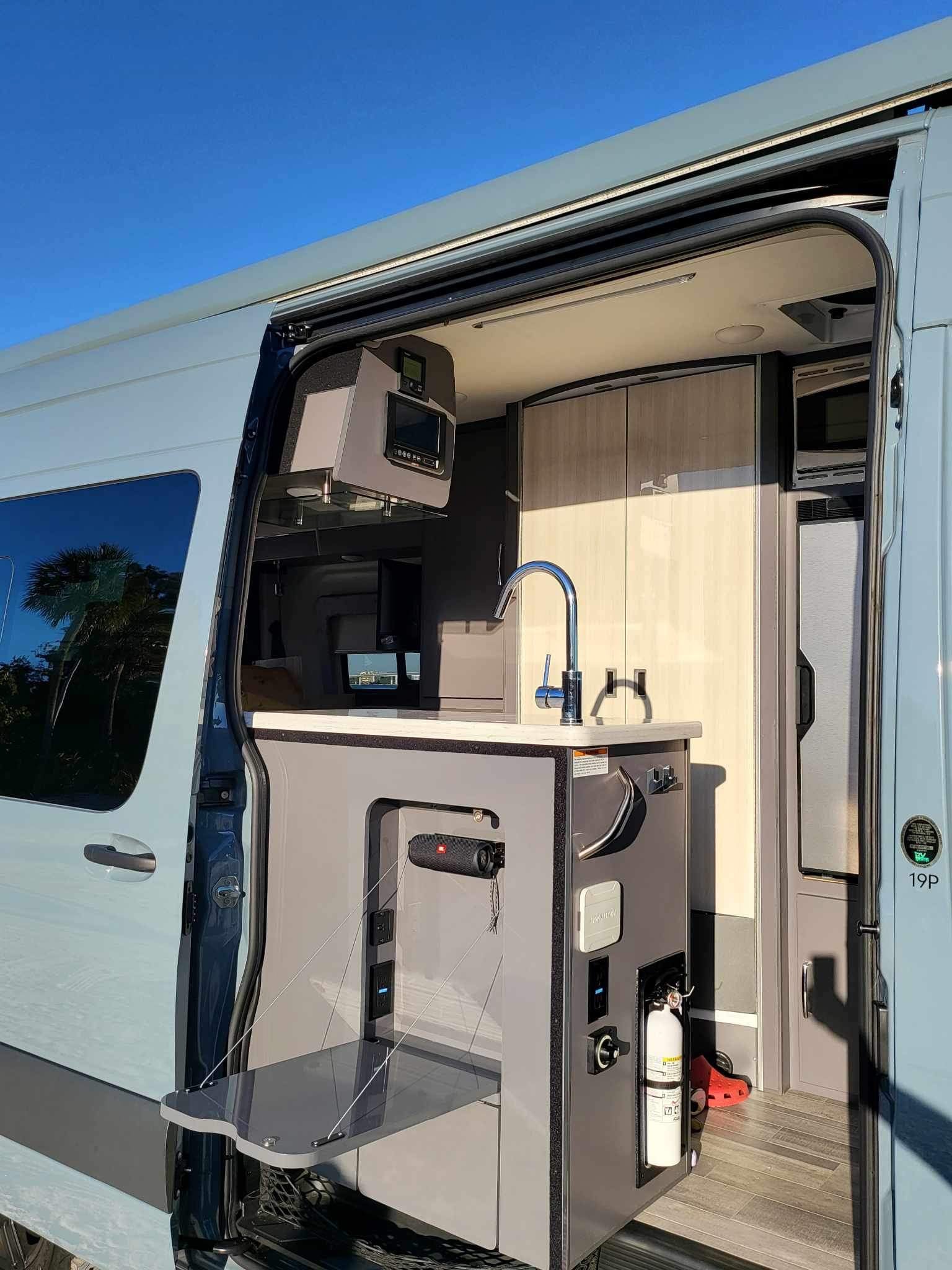 Inside a modern RV rental: compact kitchen with sink, control panel, and pull-out table for efficient mobile living.