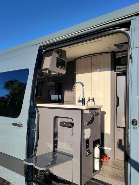 Inside a modern RV rental: compact kitchen with sink, control panel, and pull-out table for efficient mobile living.