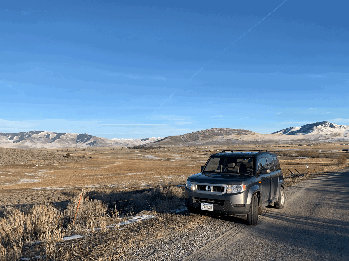 Dark grey Honda Element parked on a rural gravel road with snowy mountains. A rugged vehicle, great for an RV rental adventure.