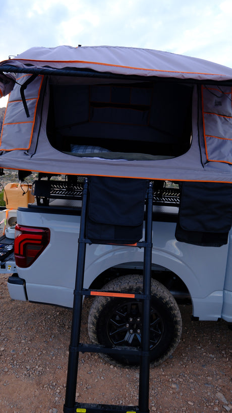 A deployed rooftop tent on a gray pickup truck, with a ladder extending to a cozy bed. Great for an RV rental outdoor adventure.