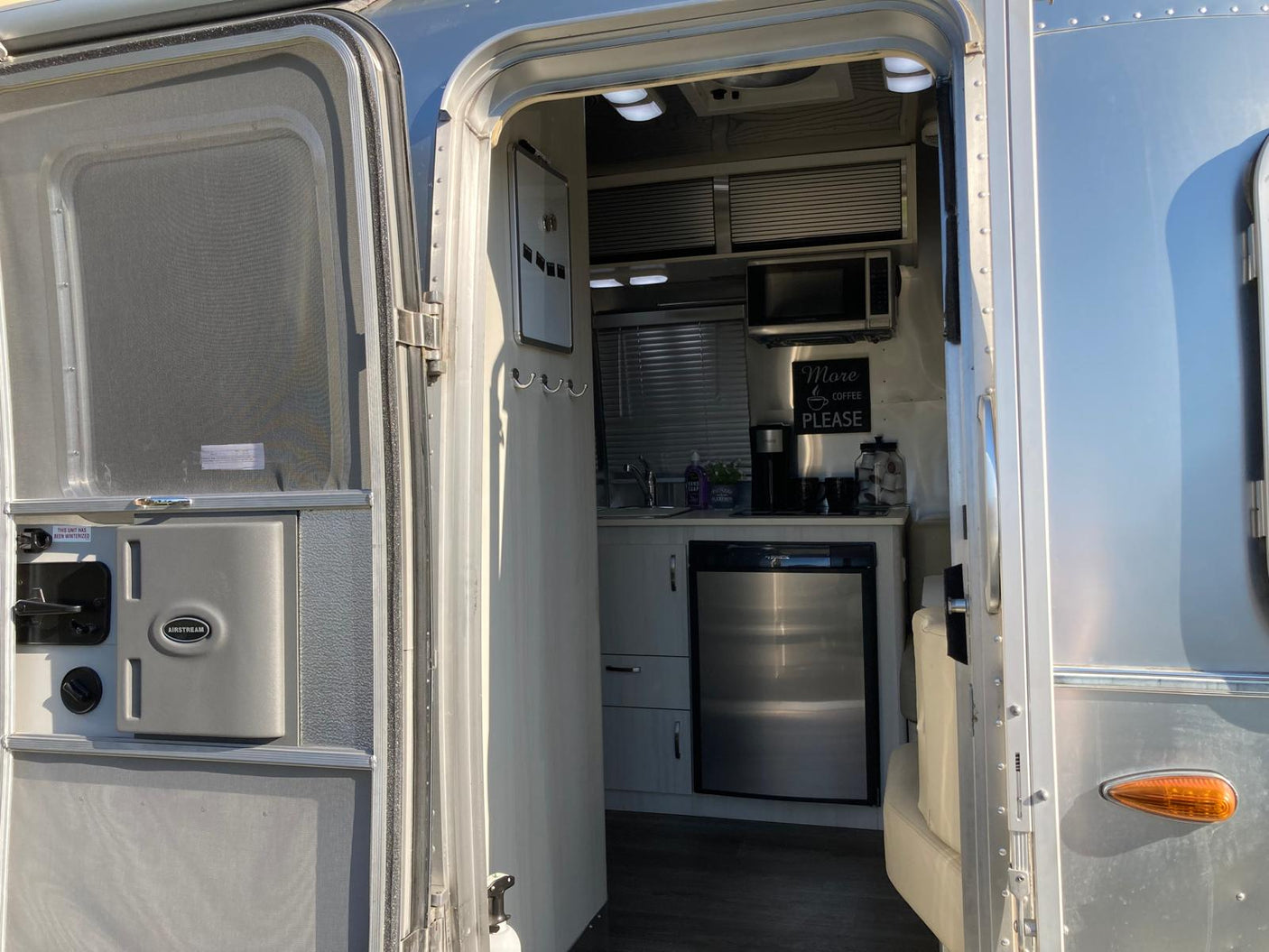 An open door reveals the stylish kitchen of an Airstream rv rental, featuring a microwave, coffee setup, and fridge.