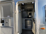 An open door reveals the stylish kitchen of an Airstream rv rental, featuring a microwave, coffee setup, and fridge.