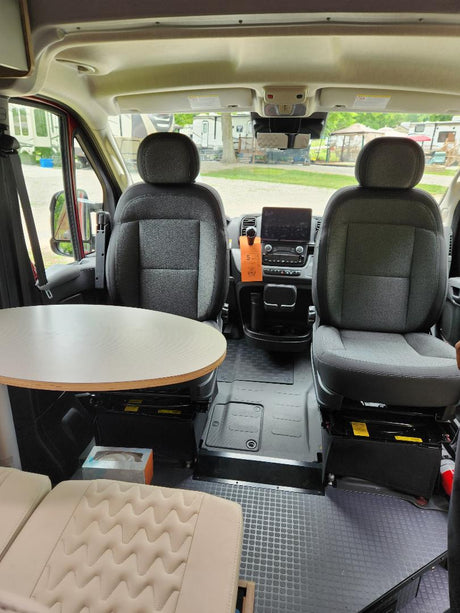 RV rental interior: driver and passenger seats, dashboard display, and a small dinette table in a comfortable camper van.