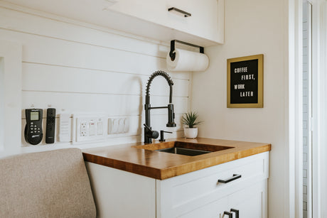 RV rental: Modern kitchenette with black faucet, wood counter, smart controls, and "Coffee First" sign for compact living.
