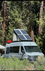 Gray RV rental camper van, pop-top with solar panels, parked among tall trees and grass. Perfect for nature camping.