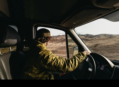 Driving an RV rental through a vast, arid landscape of rolling hills. A person in a van enjoys sunlit desert views.