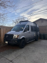A sleek gray Mercedes Sprinter camper van, equipped with a roof rack and ladder, parked on a driveway. Perfect for an RV rental adventure!