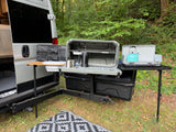 RV rental outdoor kitchen setup! Rear of a camper van with Yakima gear: stove, French press, kettle, & organized storage for camping.