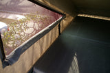 Inside an RV rental, a comfy sleeping area with a mesh window showing sunlit white flowers. Great for a camping trip.