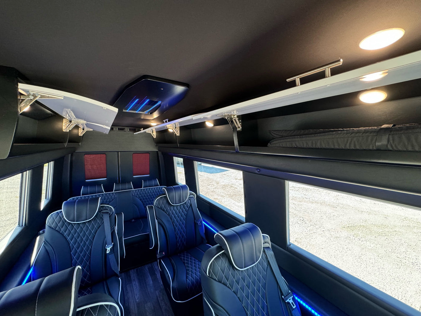 Plush, quilted seats and overhead storage inside a modern RV rental, enhanced by soft lighting. Ideal for group travel.