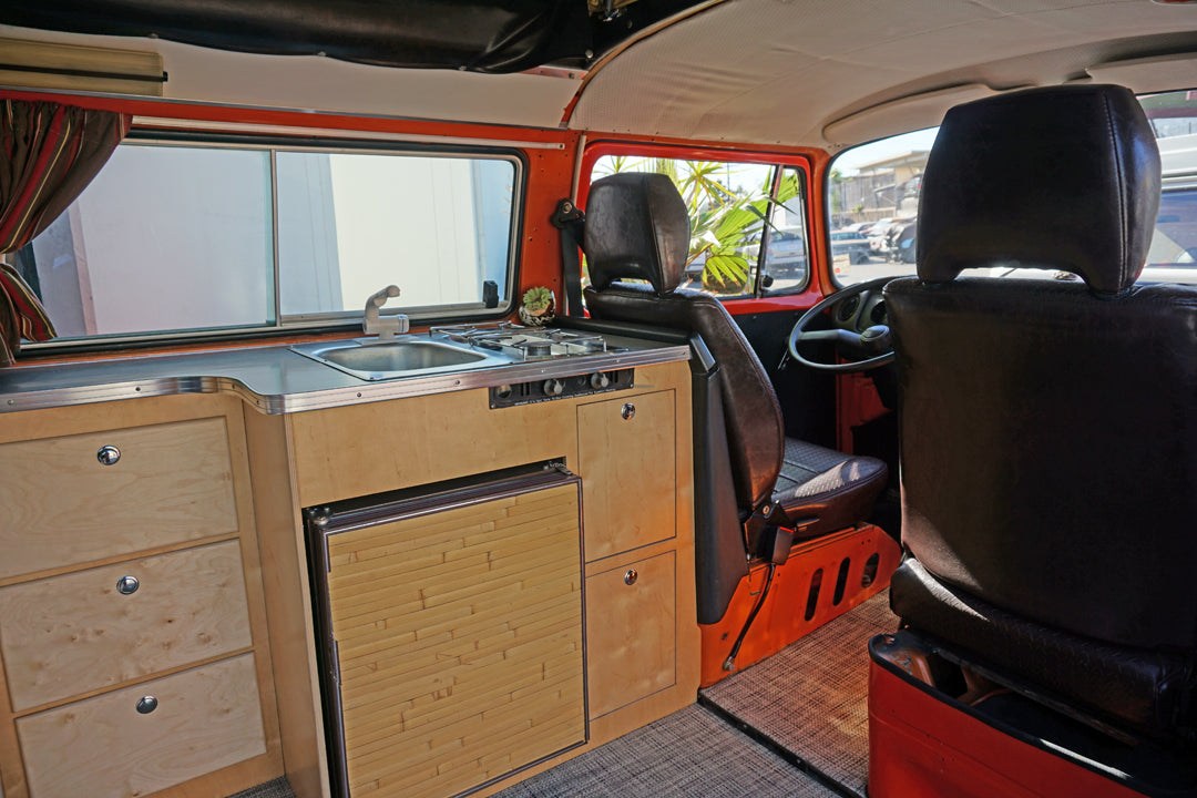 Inside this RV rental, a built-in kitchen features a sink, stove, and refrigerator, with wood cabinets and front seats visible.