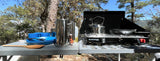 Enjoy camping meals with our RV rental! Outdoor kitchen includes a portable stove, kettle, French press, and blue dishes.