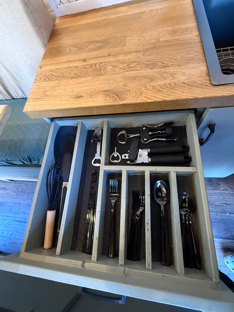 Organized kitchen drawer in an RV rental, featuring whisks, spatulas, bottle openers, corkscrews, and cutlery for your trips.