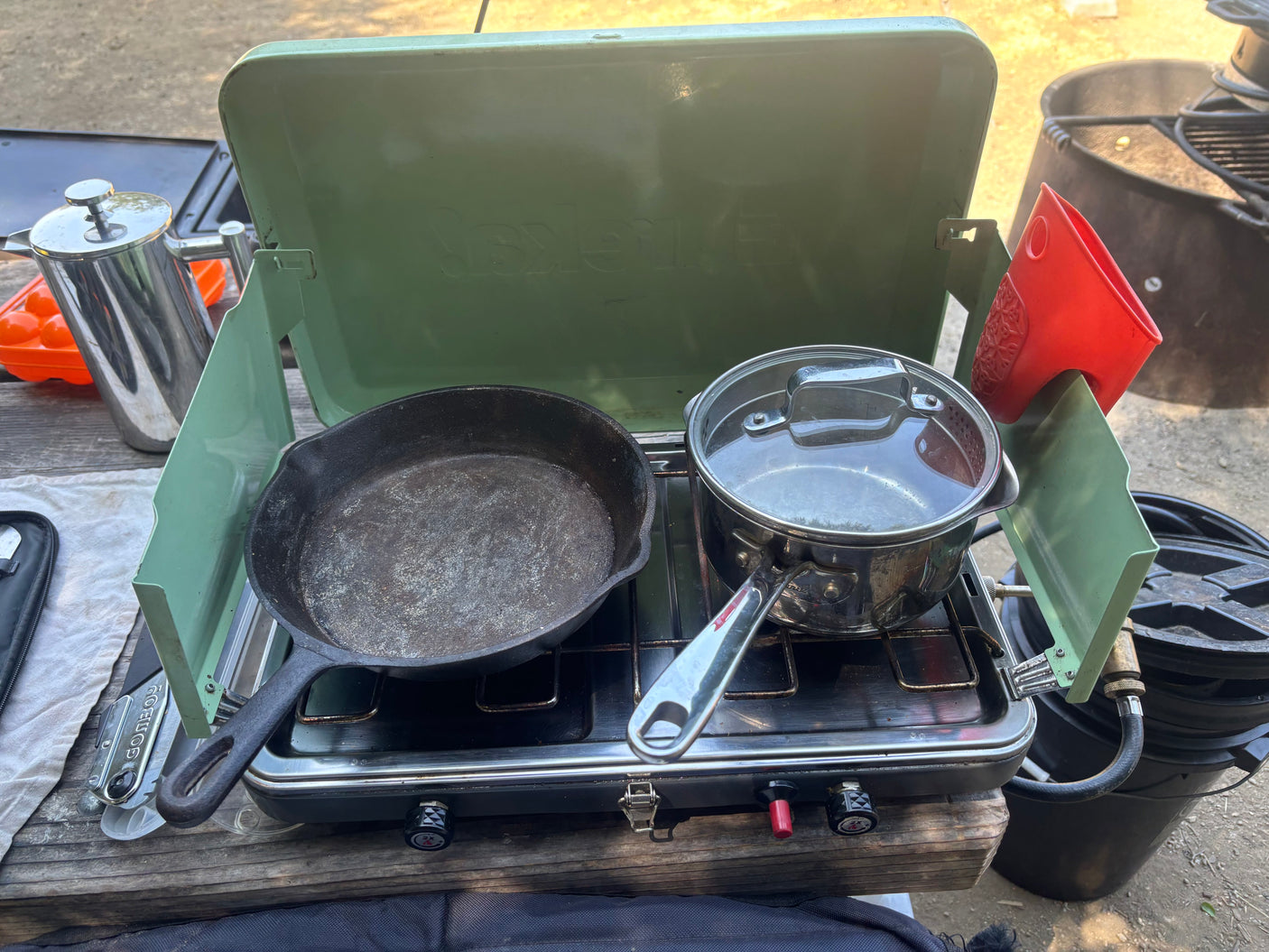 RV rental camping cookout: a portable stove with a cast iron skillet, pot, and French press on a picnic table.