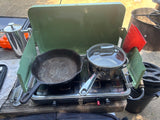 RV rental camping cookout: a portable stove with a cast iron skillet, pot, and French press on a picnic table.