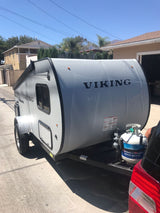 Viking travel trailer, a light gray RV rental, parked on a sunny day. Propane tank at front, ready for camping adventures.