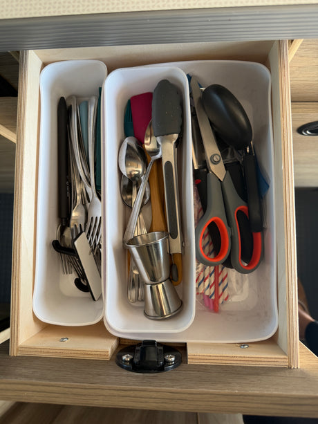 RV rental kitchen drawer with organized utensils: forks, spoons, jigger, scissors, and straws in white organizers.