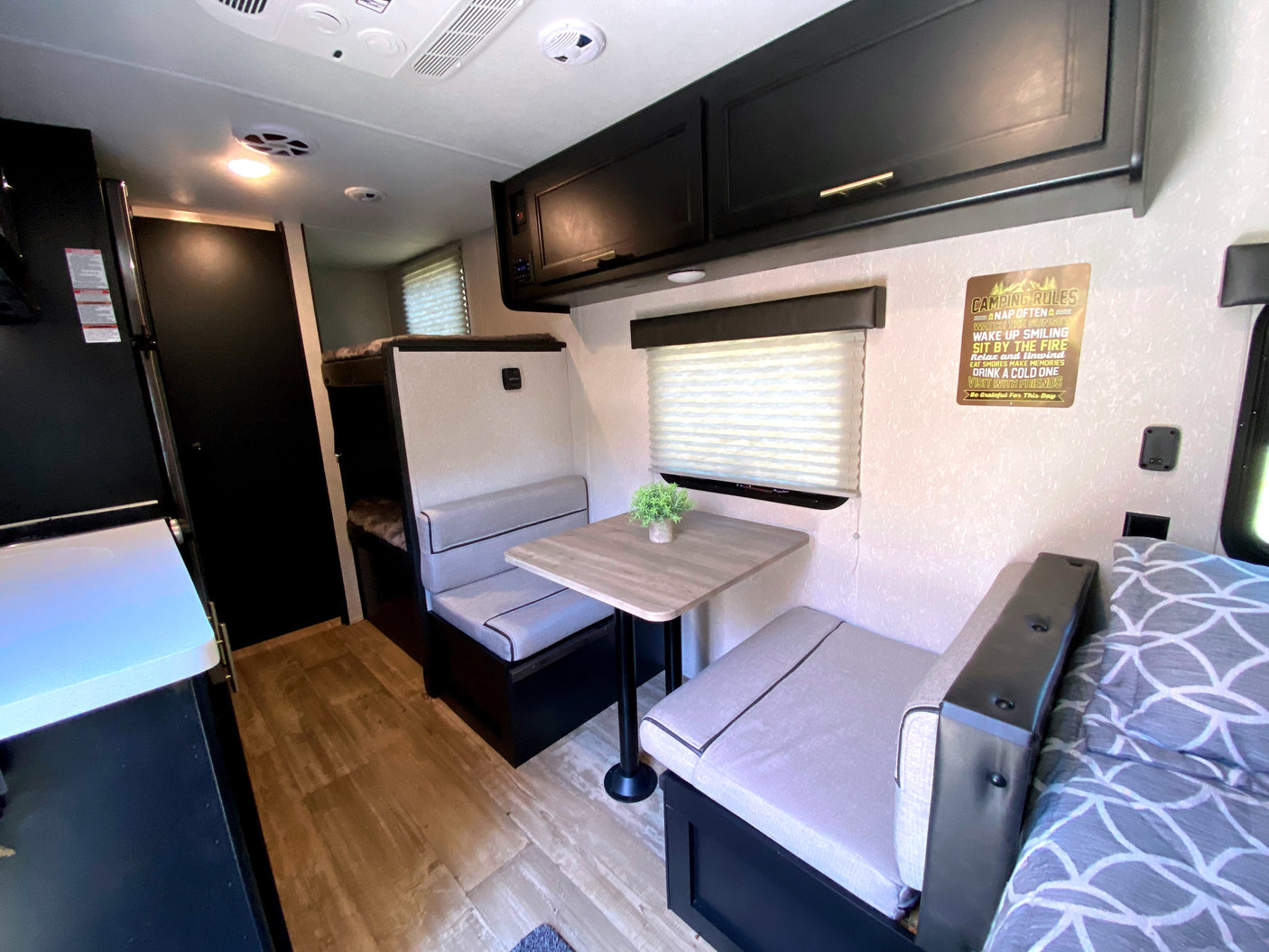 Explore this modern RV rental interior featuring a dinette, bunk beds, kitchen, and "Camping Rules" sign.