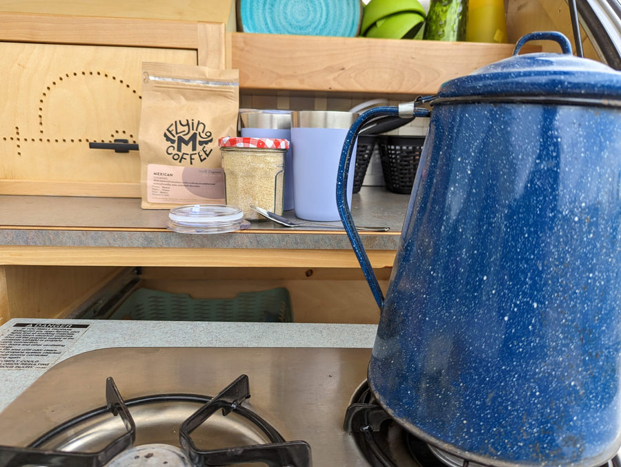 Brewing coffee in an RV rental kitchen: a blue speckled pot on the stovetop, with Flying M Coffee and sugar on a shelf.