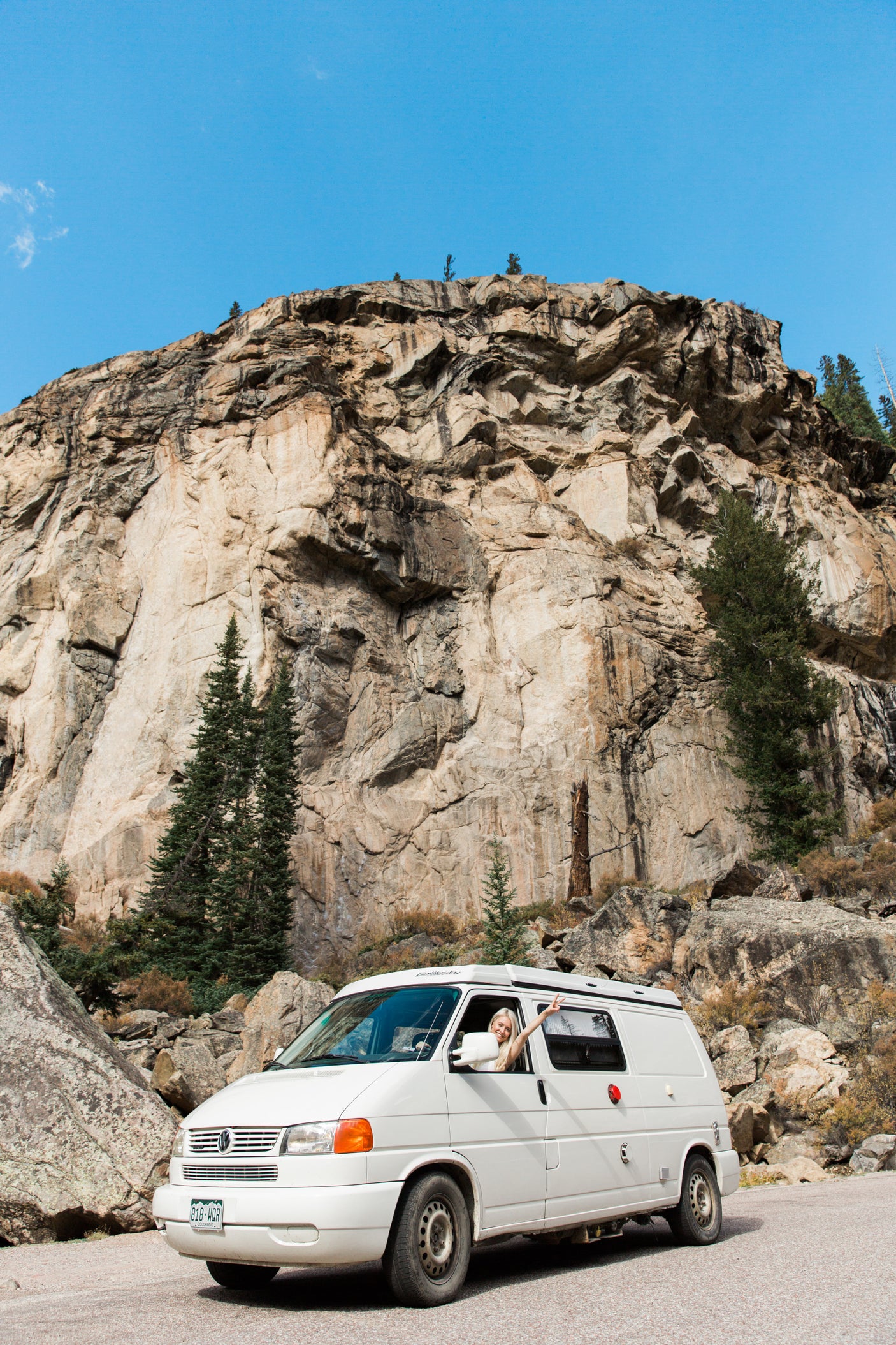 Adventure awaits! Blonde woman making peace sign from an RV rental van against a huge mountain cliff. Perfect for mountain travel.