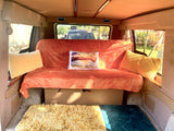 Cozy RV rental interior featuring an orange bench bed with pillows and soft floor mats, ready for travel adventures.