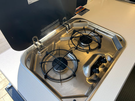 This RV rental features a compact, shiny stainless steel two-burner gas stovetop with a safety lid for cooking.