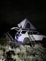 White SUV with roof-top tent & bikes at night. Perfect for rugged outdoor adventures, a unique RV rental option.