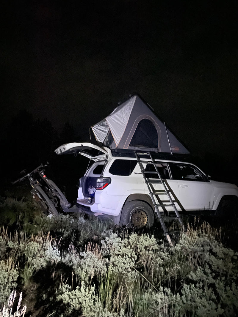 White SUV with roof-top tent & bikes at night. Perfect for rugged outdoor adventures, a unique RV rental option. — photo 17