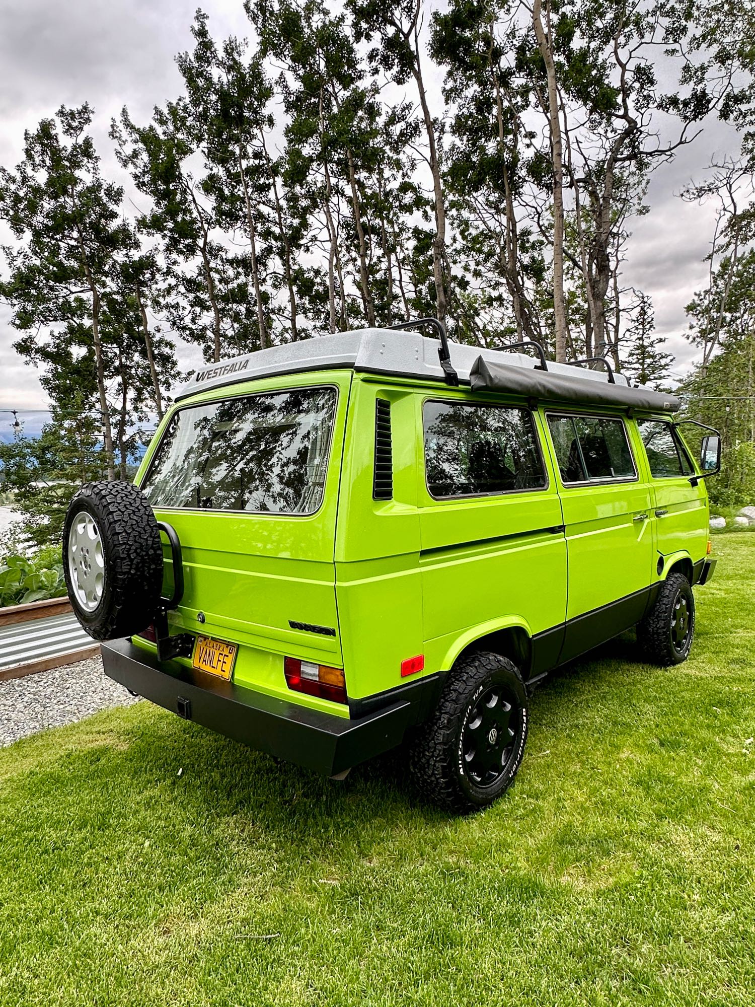 Bright green VW Westfalia camper, an ideal RV rental for Alaska vanlife adventures, parked by water.
