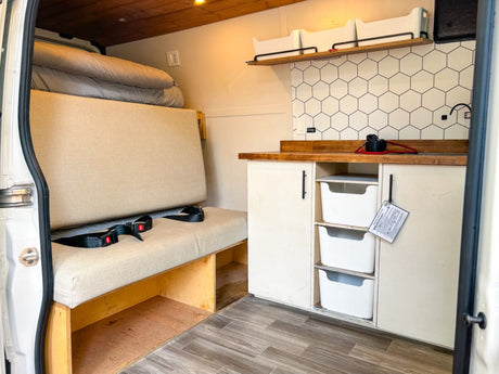 Inside an RV rental: a compact kitchenette with hex tiles, comfy bench seating, and smart storage solutions for your journey.