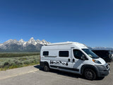 Scenic RV rental adventure! White camper van parked with stunning snow-capped mountains in the background under a clear blue sky.