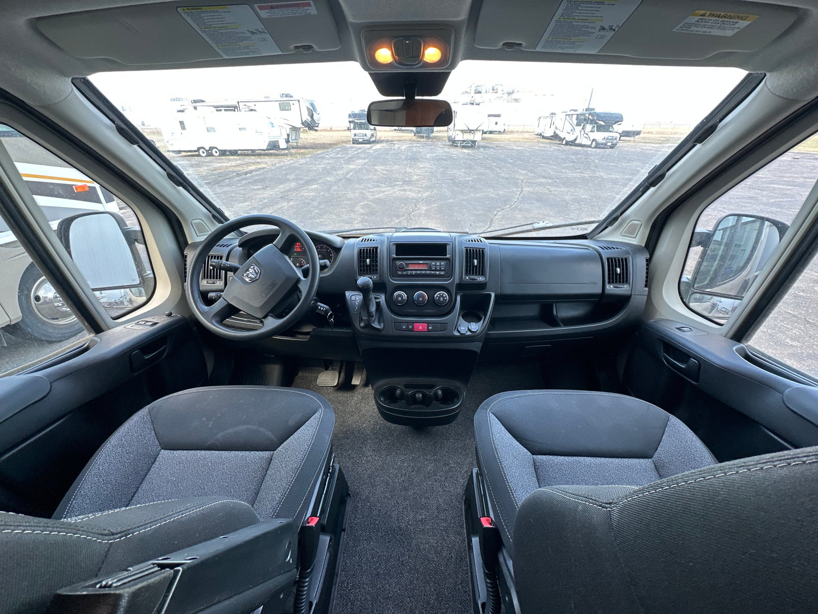 Driver's view from an rv rental van, showing the dashboard, steering wheel, seats, and a lot full of RVs outside.