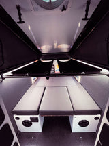 Explore the compact RV rental interior, featuring a versatile sleeping area with three gray cushions and built-in amenities.