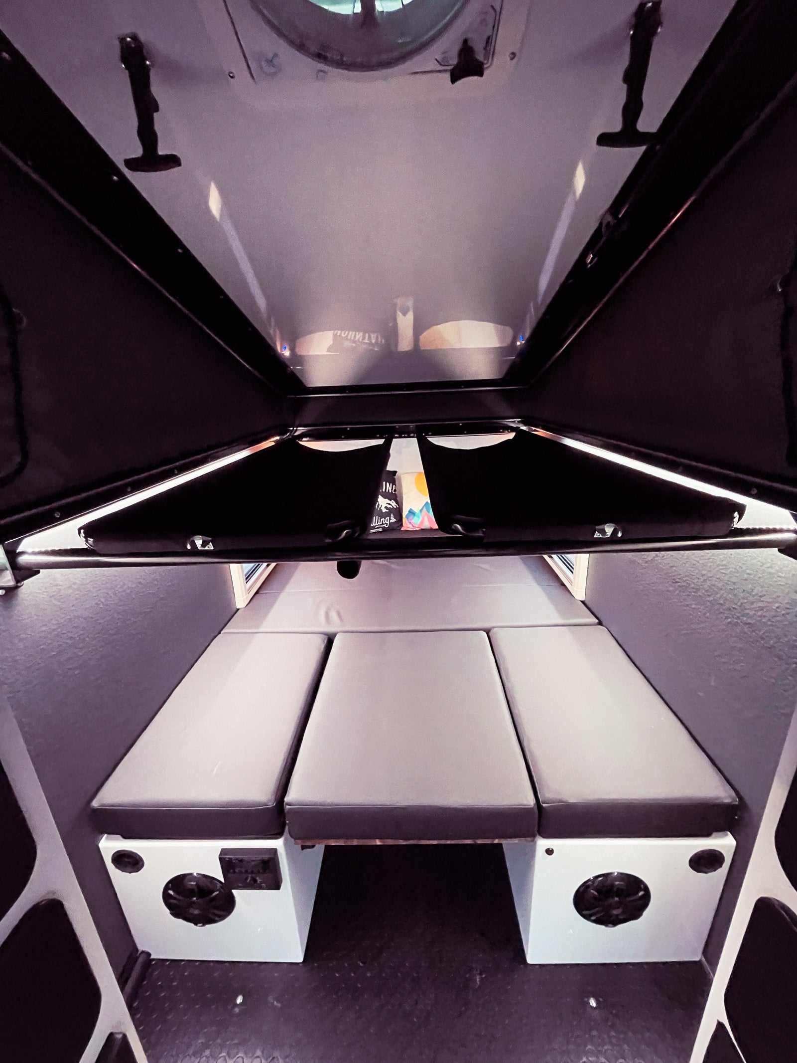 Explore the compact RV rental interior, featuring a versatile sleeping area with three gray cushions and built-in amenities.