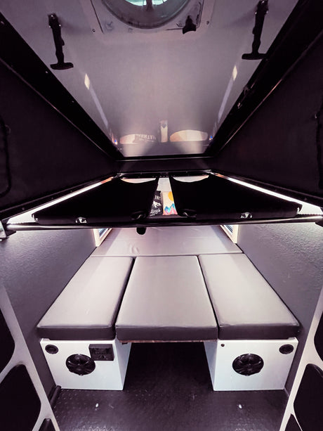 Explore the compact RV rental interior, featuring a versatile sleeping area with three gray cushions and built-in amenities.