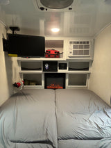 Cozy RV rental bedroom featuring a TV, AC, electric fireplace, and storage for compact travel comfort.