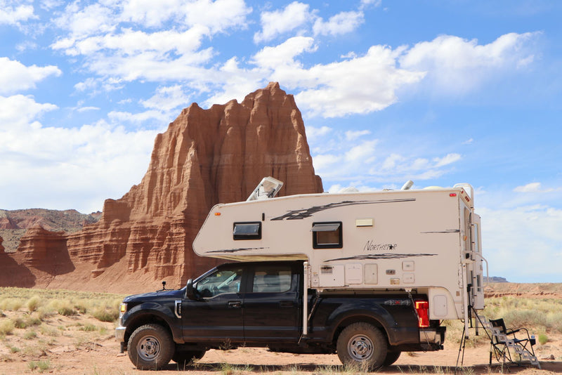 Truck camper for an RV rental adventure in a stunning desert landscape with red rock formations. Perfect for off-grid camping.|An RV rental truck camper is parked before majestic red rock formations under a blue sky — photo 1