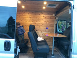 Explore this warm RV rental interior: wood walls, cozy seating, and a table. A child plays inside, a woman looks in.