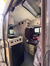 Interior of an rv rental camper van, showing a kitchenette, seating with a child seat, and various control panels.