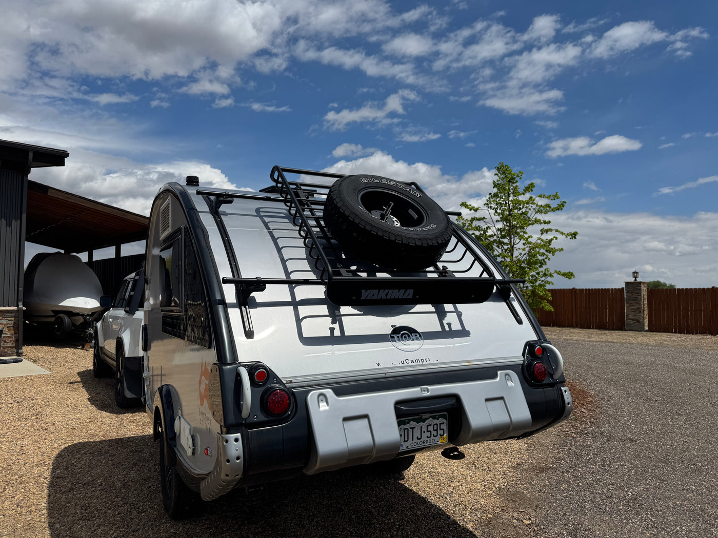 Rear view of a silver teardrop RV rental, featuring a roof rack with a spare tire and YAKIMA gear on a gravel driveway. — photo 7