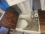 View inside an RV rental wet bath, showing a toilet, shower, and stored toiletries in a compact space.
